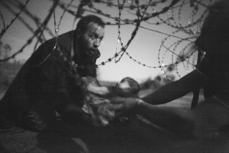 couple réfugié tentant de faire passer leur bébé sous une clôture barbelée